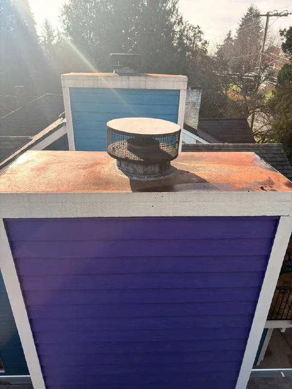 A cracked concrete chimney crown seen from the roof with a flue tile through its center