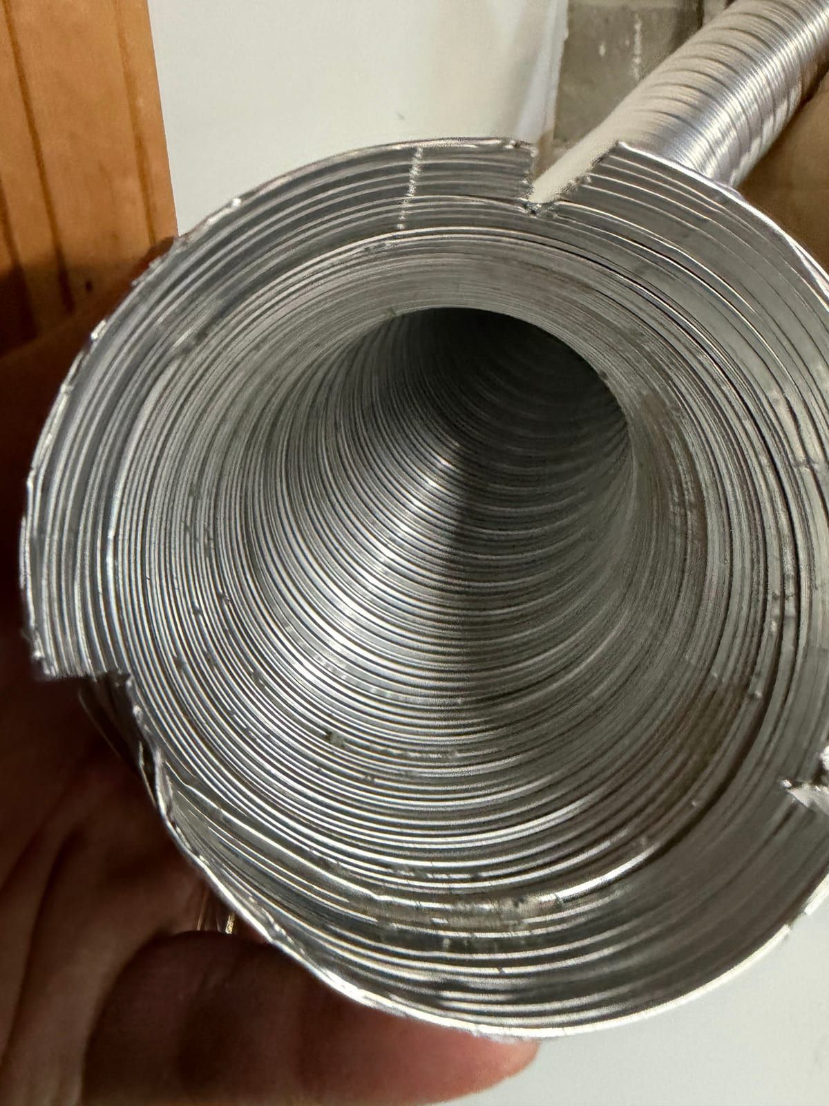 A length of flexible metal ducting held in the hand, ready to be fitted