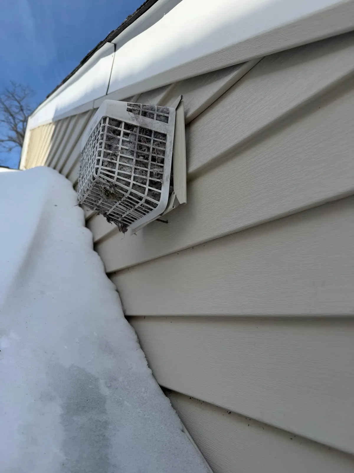 A dryer vent hood on the white siding of a New Jersey house